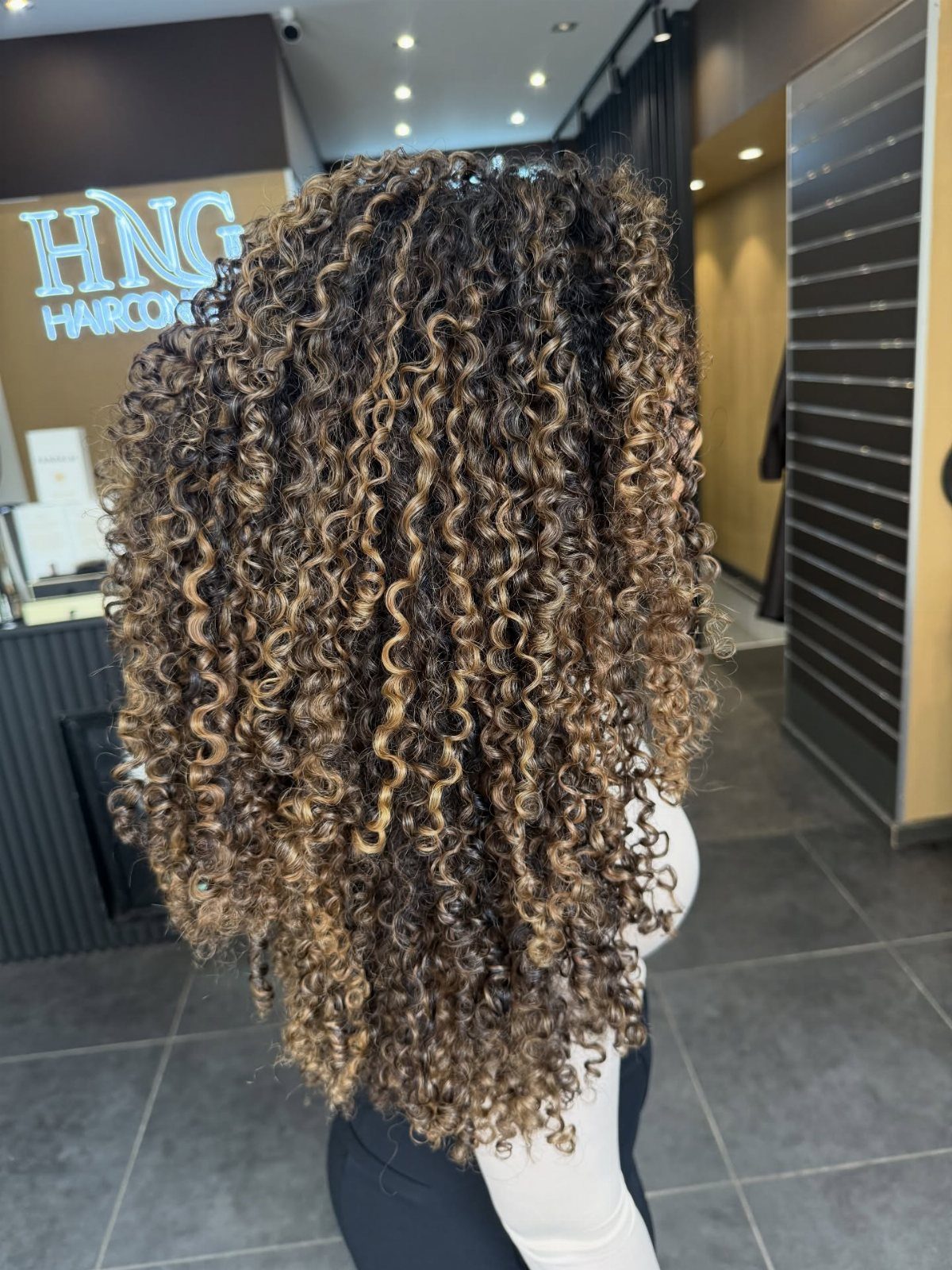 9 Long African Hair Ideas for Braids, Curls and Waves 5 Long curly hair with golden blonde highlights seen from the back in a salon