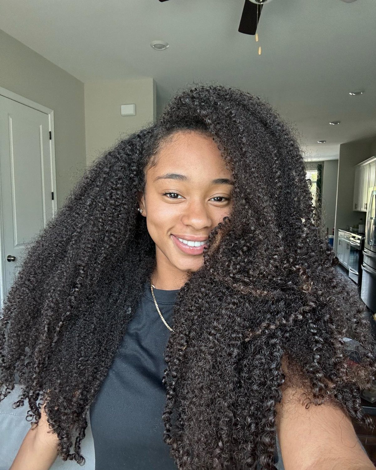 9 Long African Hair Ideas for Braids, Curls and Waves 6 Woman with long, voluminous curly black ringlets smiling for a close-up portrait.