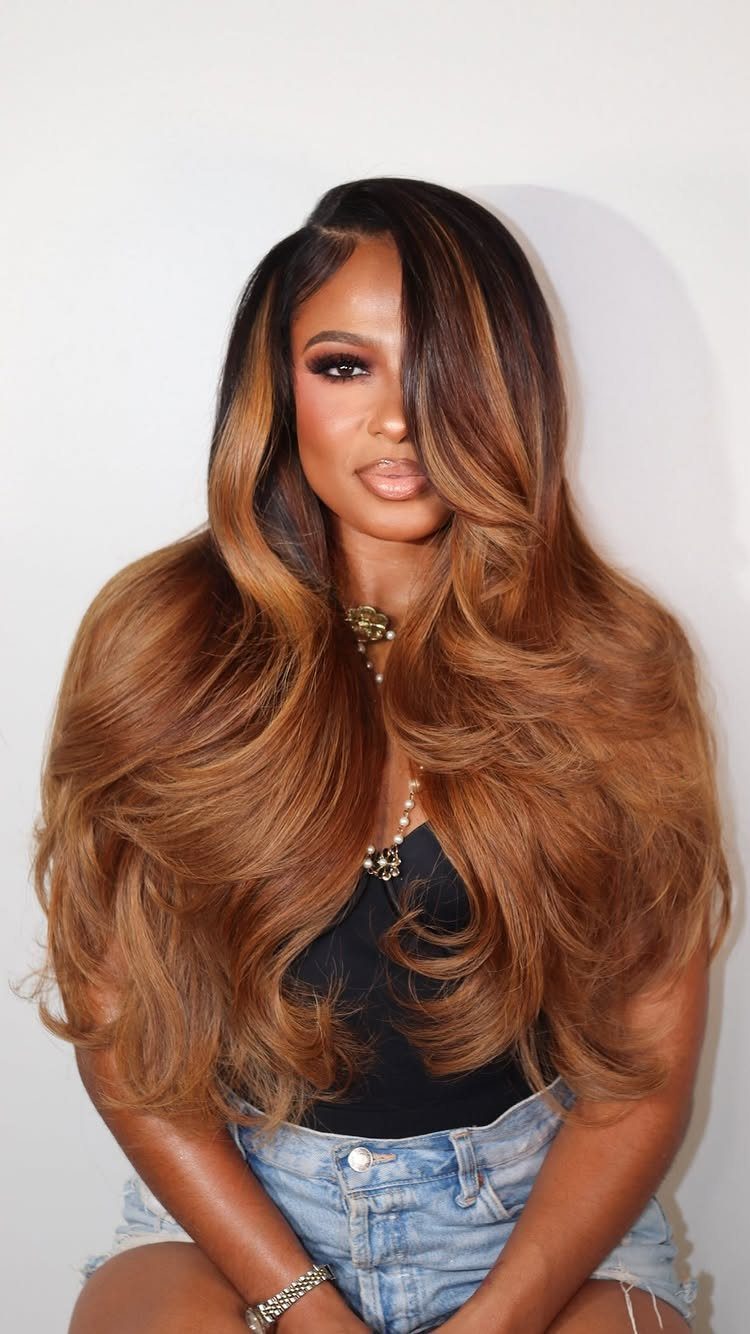 9 Long African Hair Ideas for Braids, Curls and Waves 3 Woman with long golden brown curly hair wearing a black top and denim shorts.
