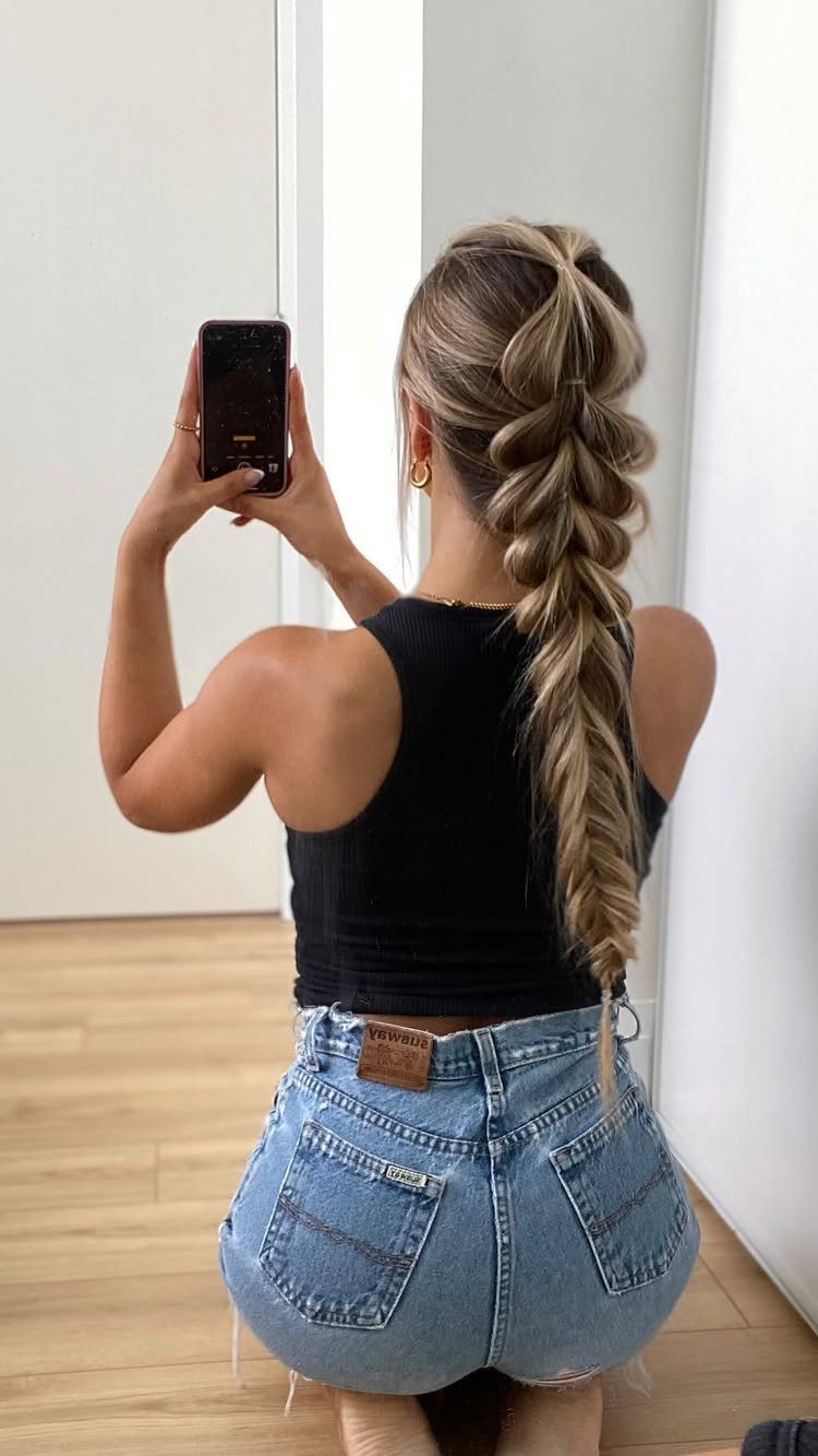 Woman with long blonde hair in a half-up braided ponytail taking a selfie.