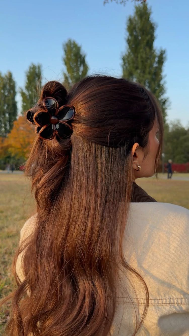 Woman with long brown wavy hair in a half-up style with flower clip