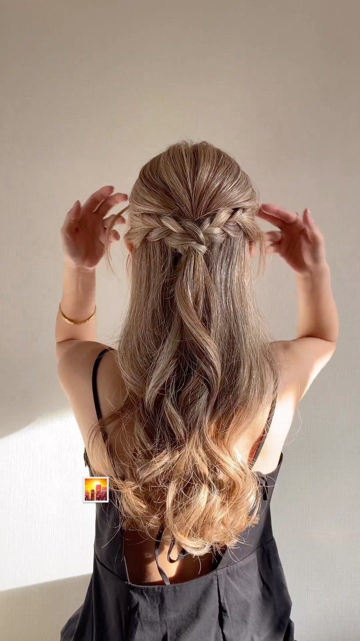 Woman with long blonde wavy hair in a half-up braided hairstyle from behind