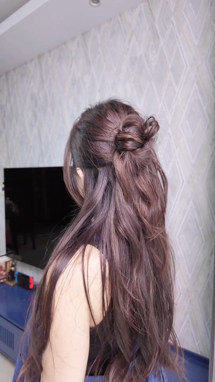Woman with long wavy brown hair styled in a half-up bun from behind
