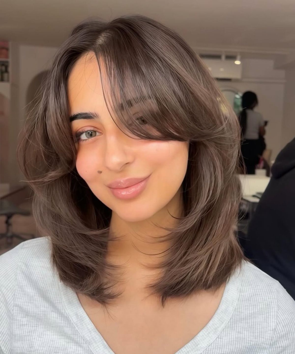 9 Medium Length Perm Hair Ideas with Waves and Curls 9 Woman with medium length brown hair styled in voluminous permed waves and bangs.