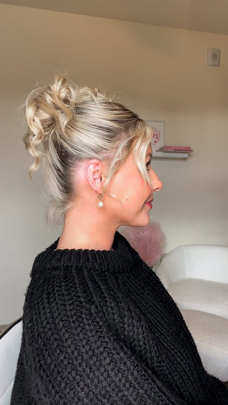 Woman with blonde hair styled in a messy high bun wearing black sweater