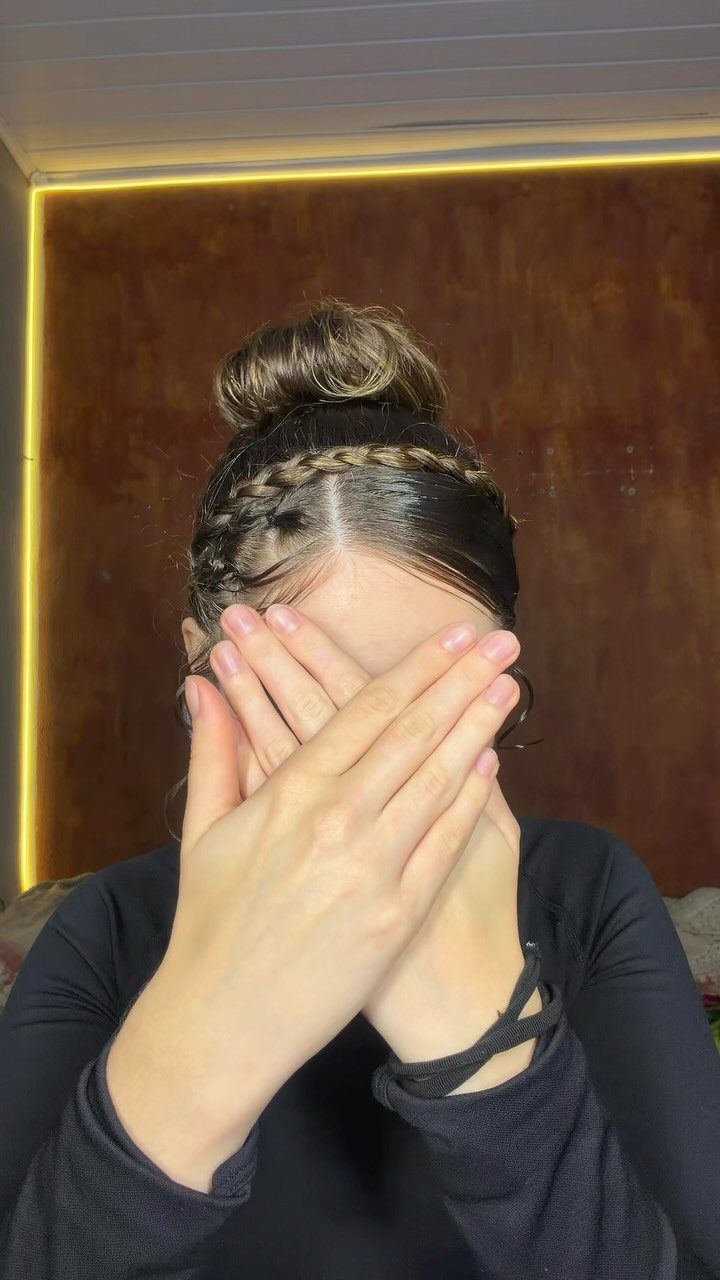 Person with a high messy bun and a braided headband covering their face.