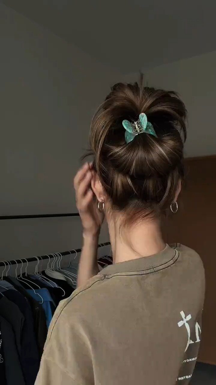 Brown hair styled in a high messy bun secured with a teal clip.