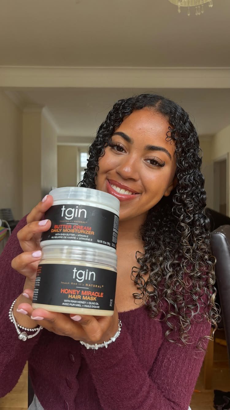 Woman with curly hair holding tgin Butter Cream Daily Moisturizer and hair mask jars.