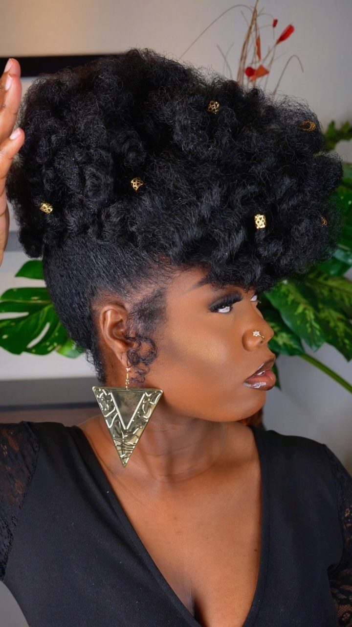 Woman with a voluminous natural black hair pompadour updo and gold jewelry accents.