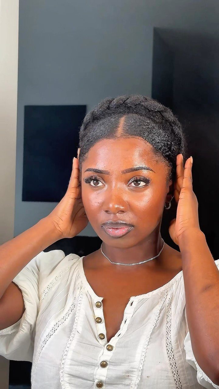 Black woman with a crown twist updo and a white button-down blouse.