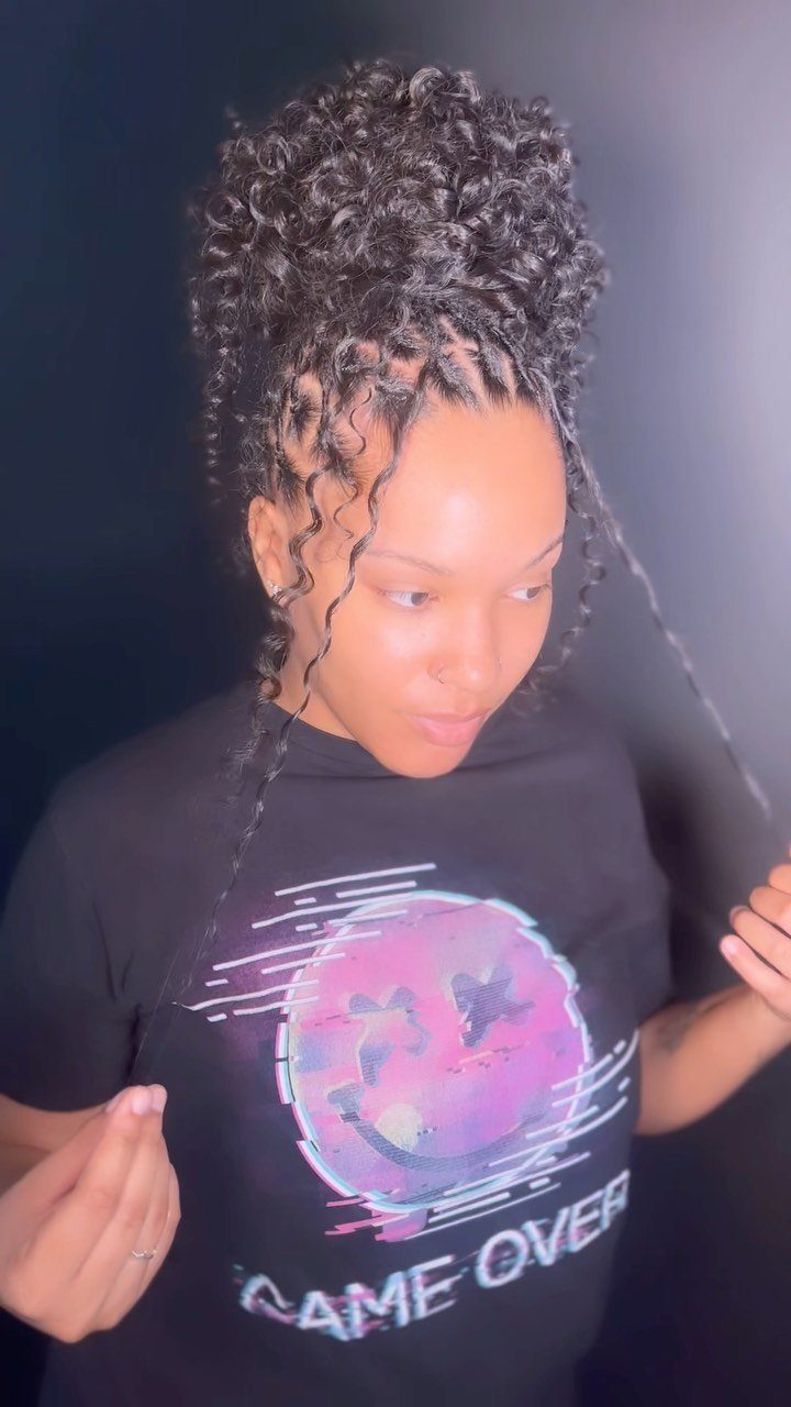 Woman with a high curly bun and thin side braids framing her face.