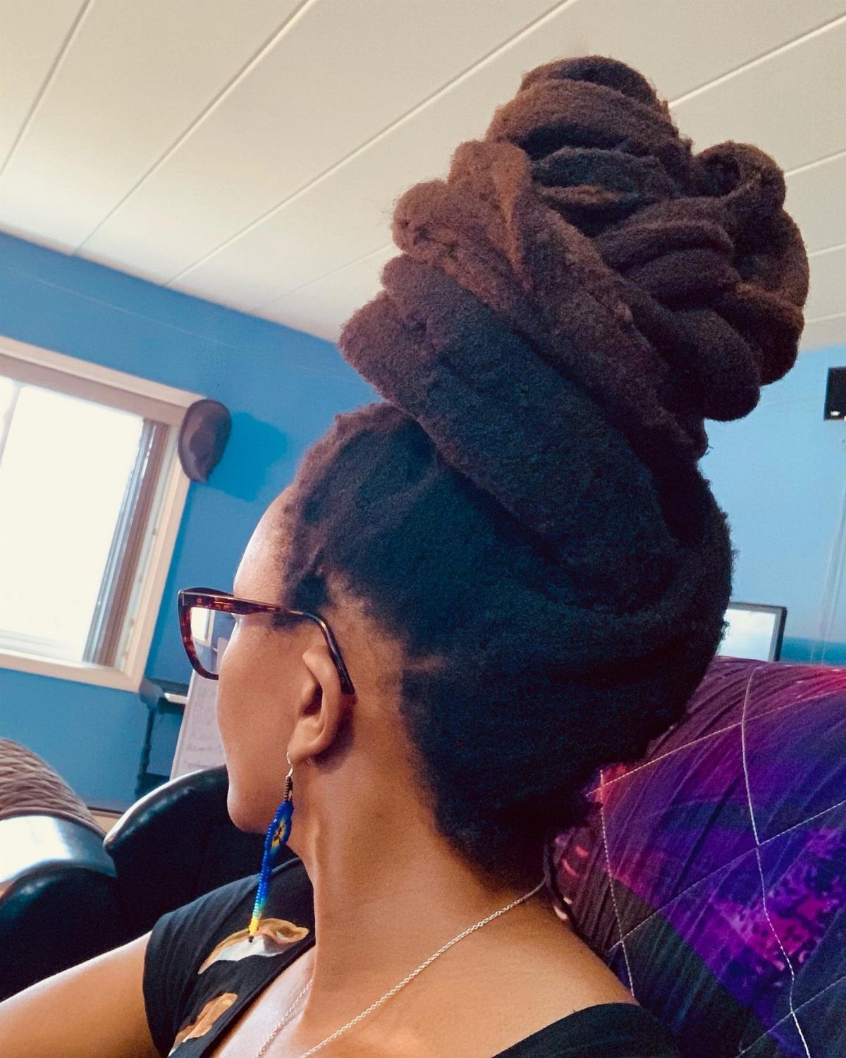 Woman with dark brown dreadlocks styled into a large, high coiled bun updo.