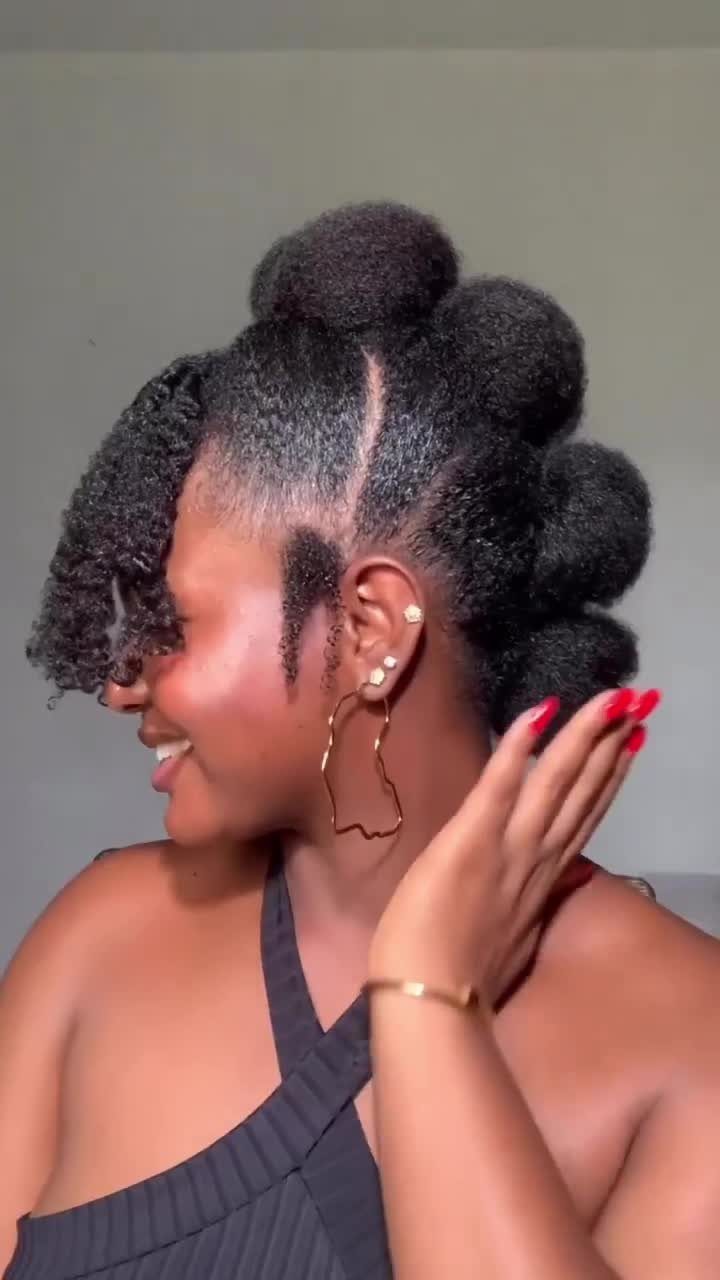 Woman with natural black hair styled in a hat-shaped updo with curly bangs.