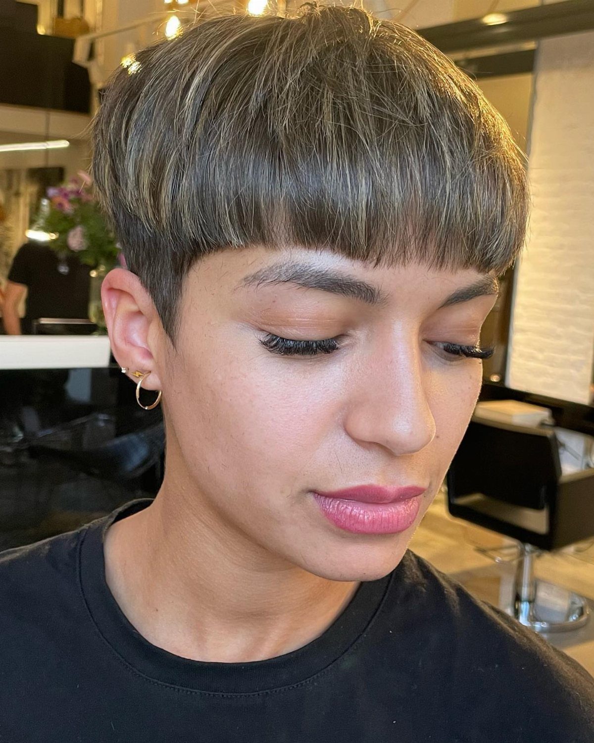Person with a short brown bowl cut hairstyle and blonde highlights in a salon.