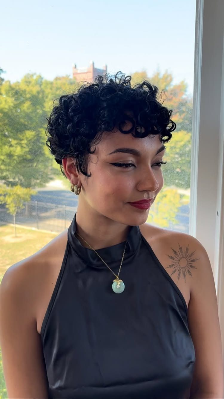 Woman with short curly black hair wearing a black halter top by a window