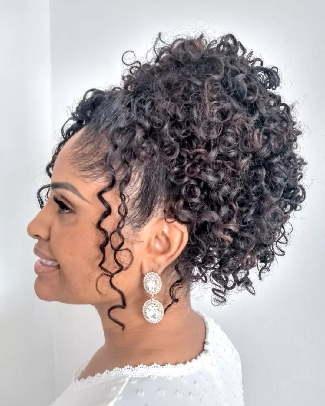 Woman with dark curly hair styled in an elegant updo and sparkling earrings.