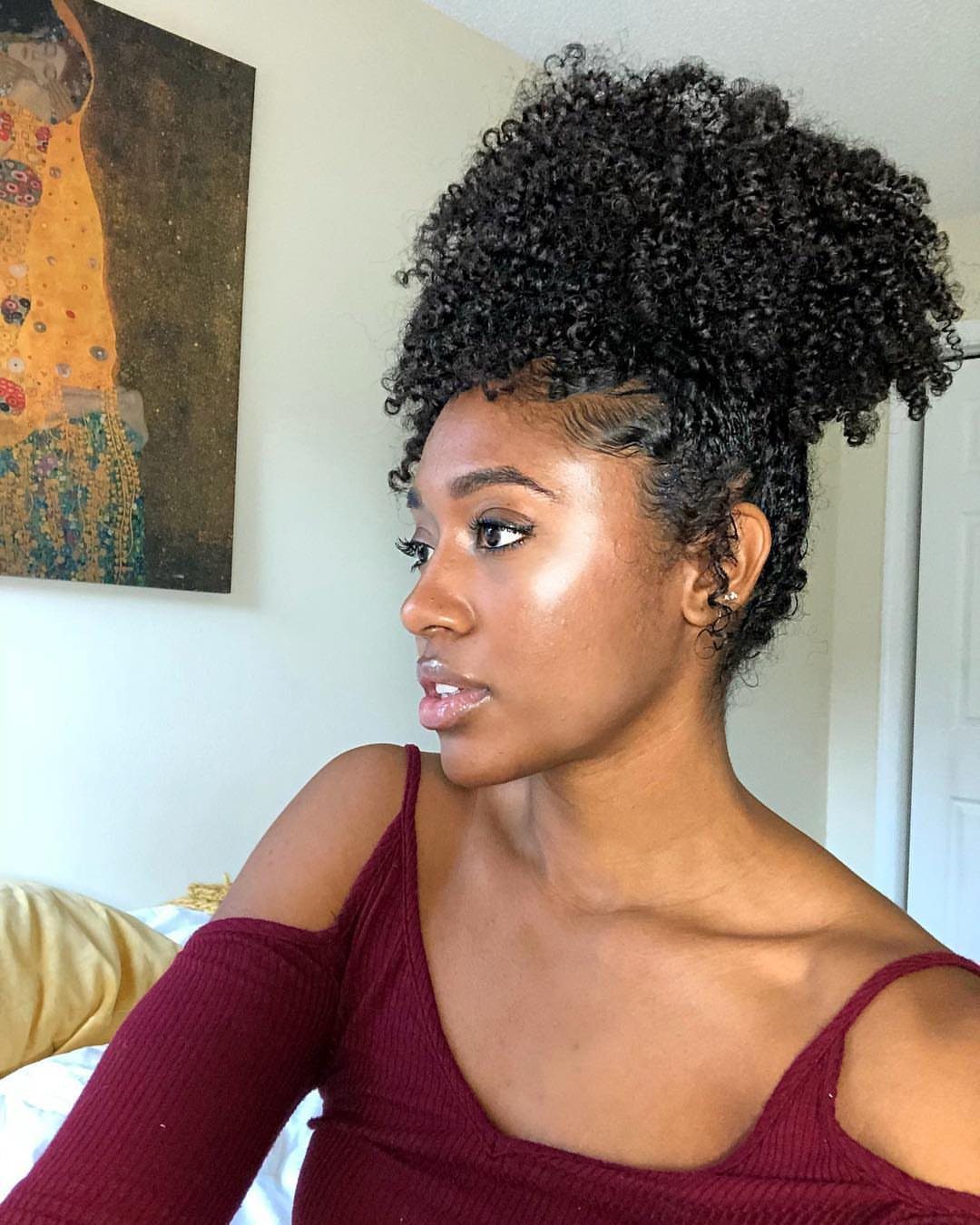 Woman with curly hair styled in a high pineapple ponytail wearing maroon top.