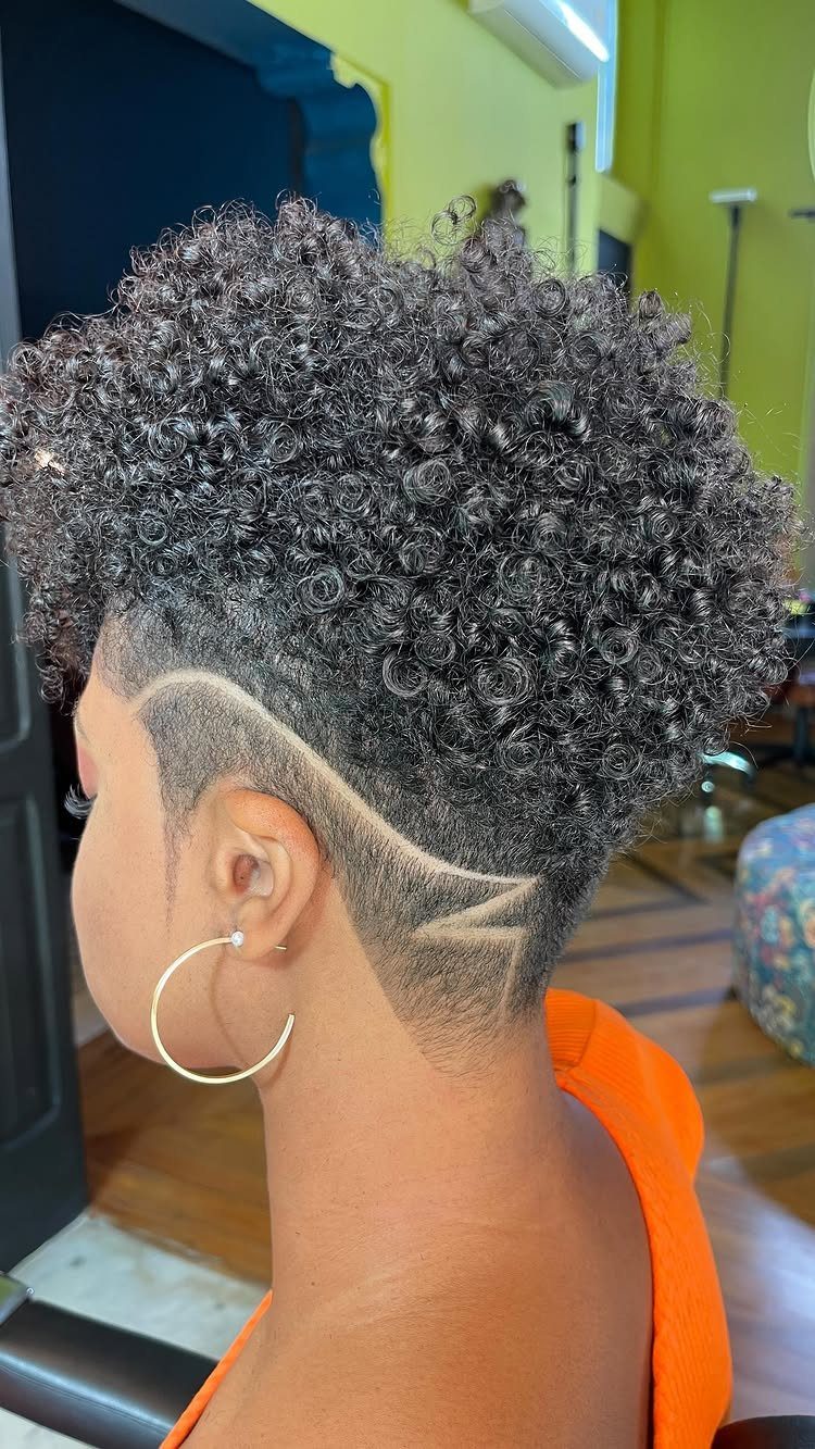 Person with short curly black hair and a shaved geometric design on the side.