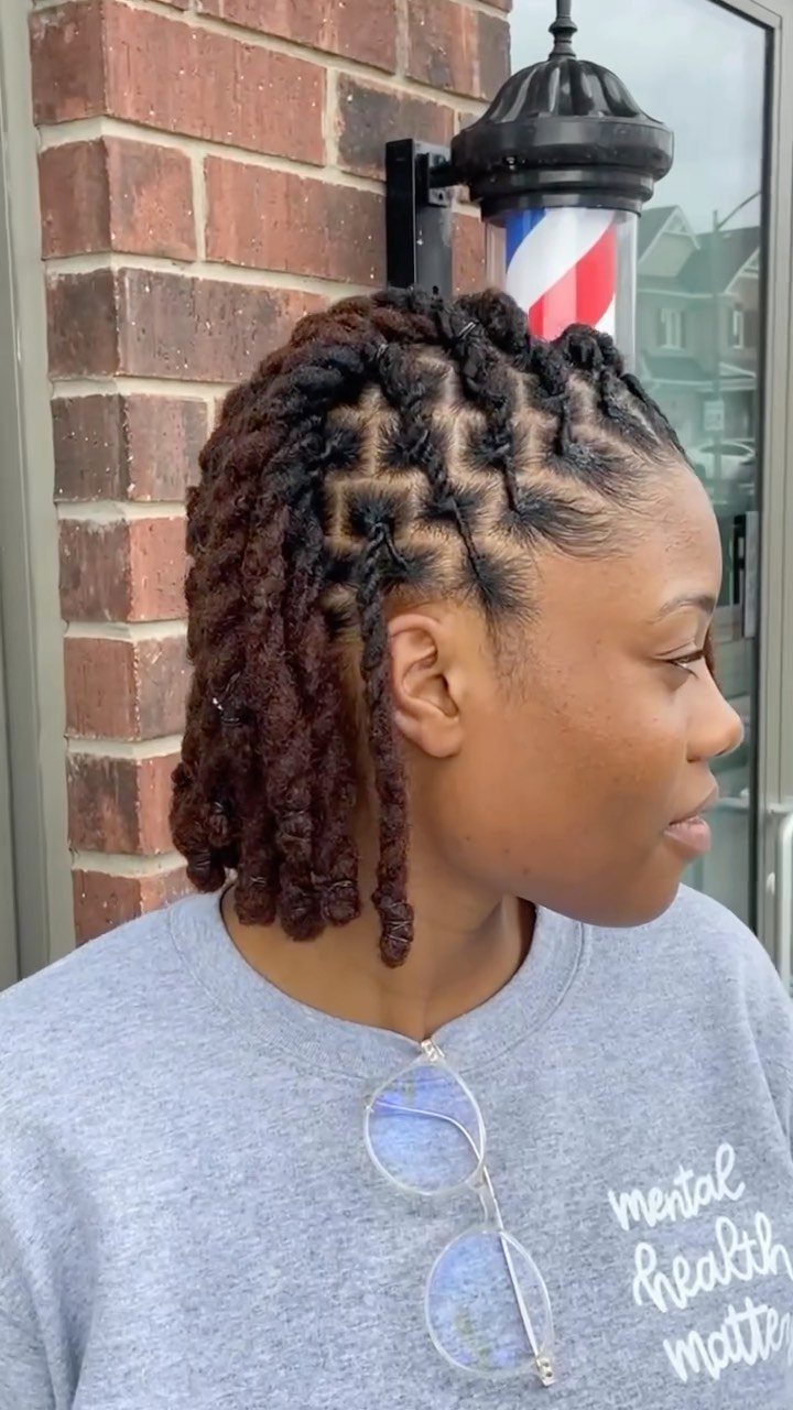 Woman with brown starter locs and patterned parting standing by a barber pole.