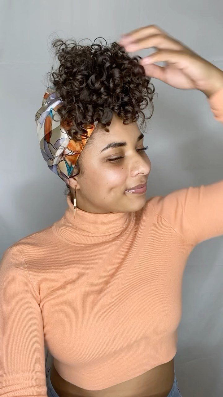 Woman with defined curly short hair wearing a colorful headwrap and peach top.