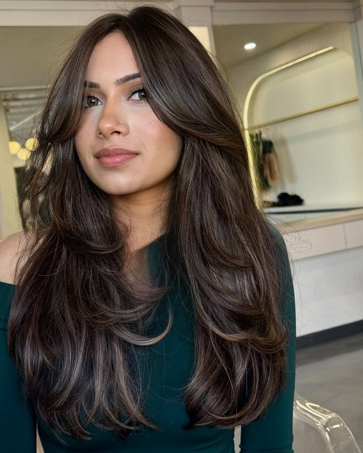 Woman with long, wavy ashy dark brown hair wearing a dark green top.