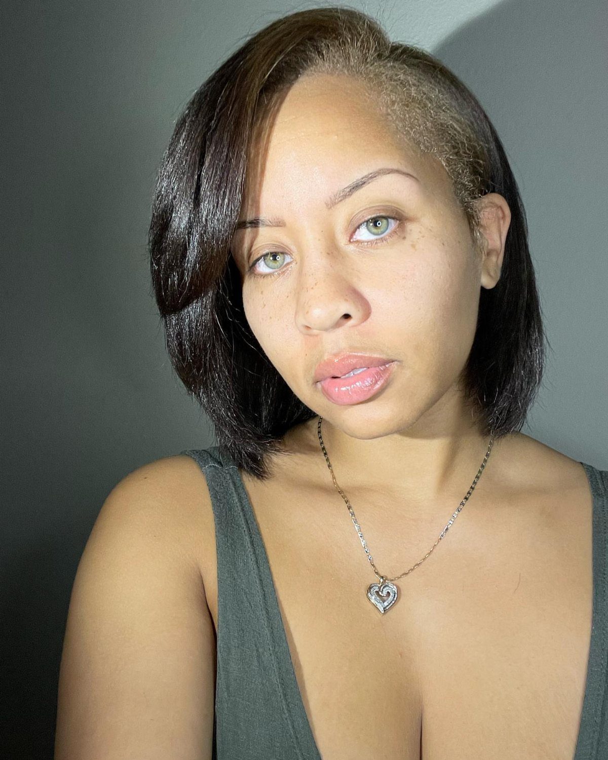 Woman with dark black-brown hair and green eyes wearing a heart pendant necklace.