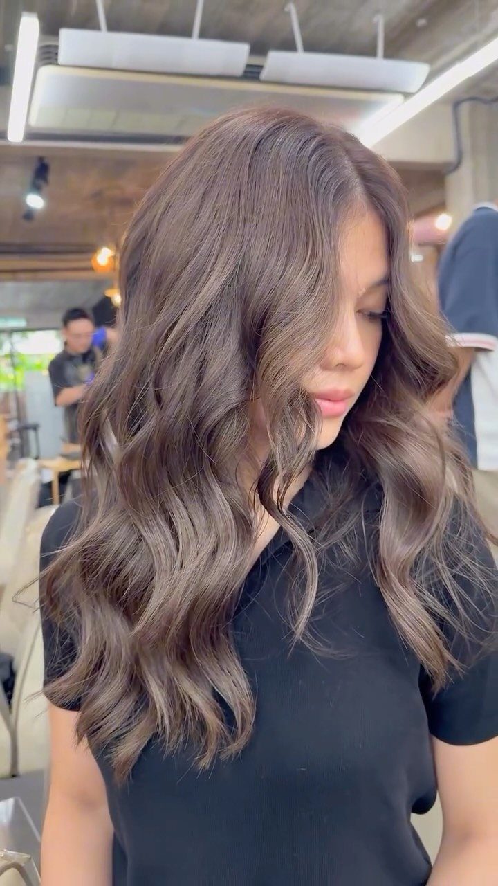 Woman with long wavy mushroom brown hair wearing a black shirt indoors.
