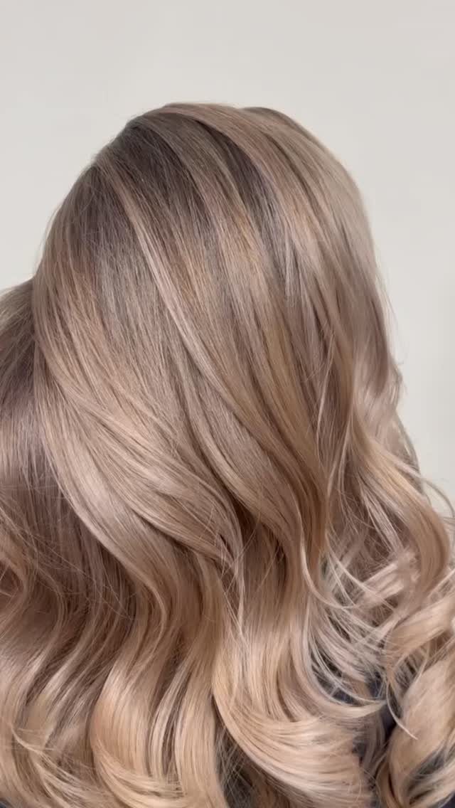 Long wavy hair with neutral balayage blending ash brown into sandy blonde tones.