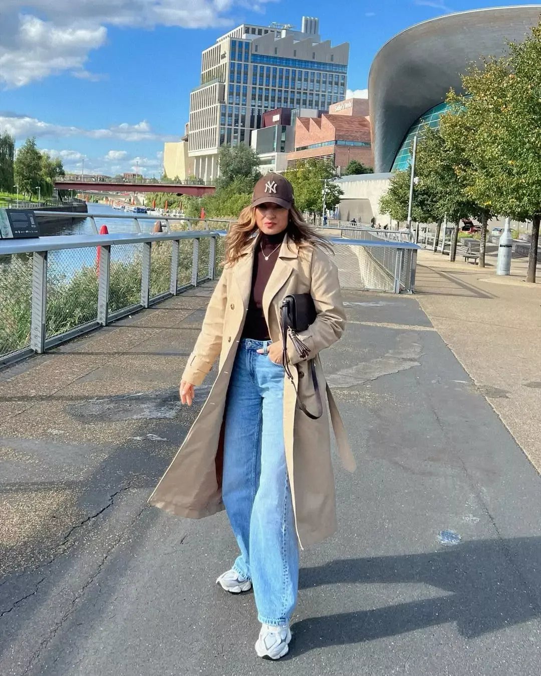 Woman wearing wide-leg denim jeans and chunky white sneakers on a city walkway.