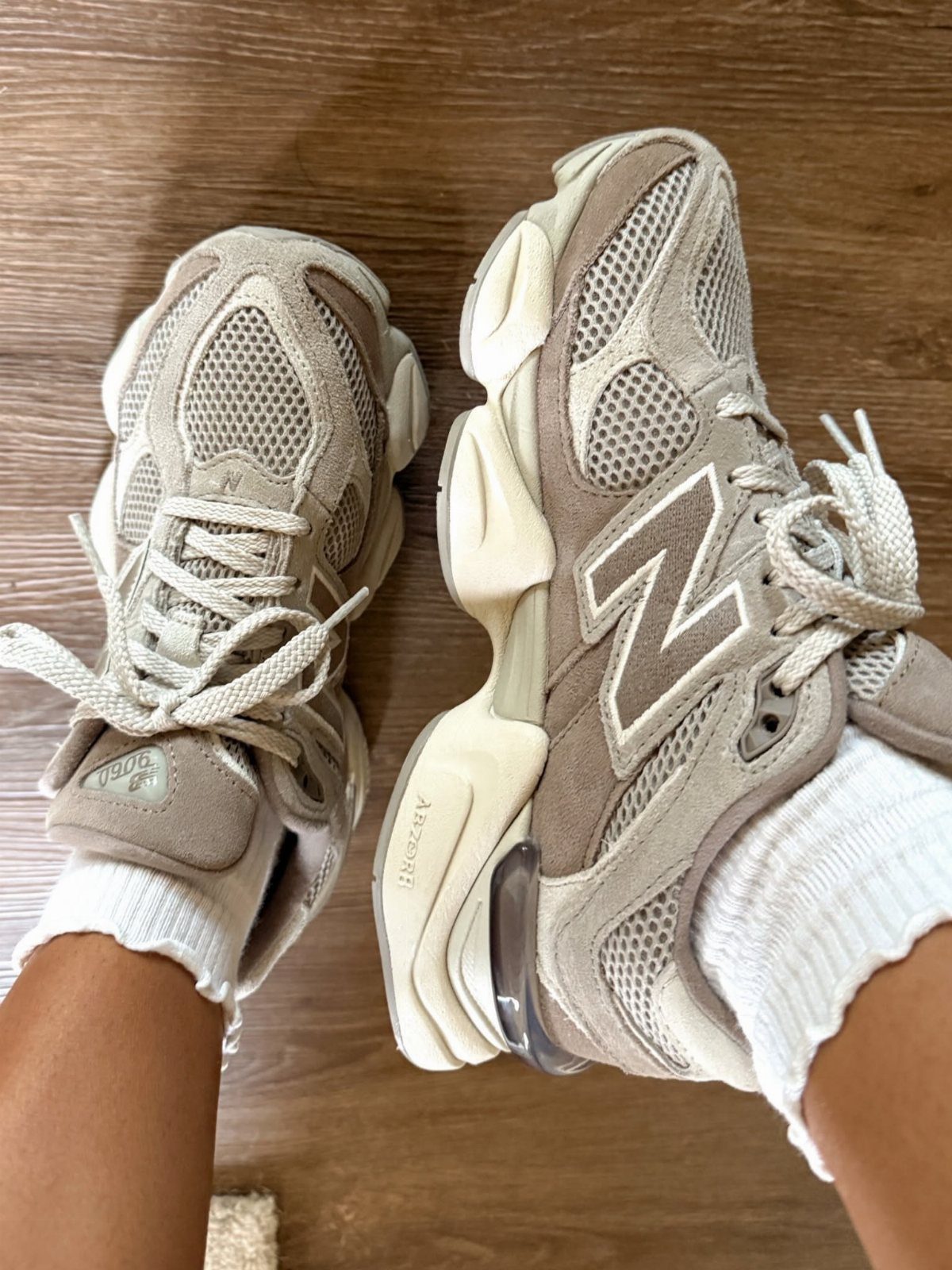 Truffle beige New Balance 9060 sneakers worn with white socks on wooden flooring.