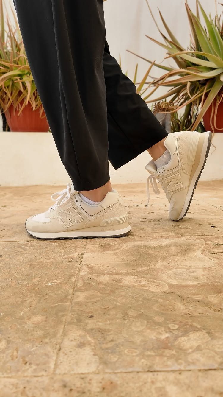 New Balance Shoes Beige: 5 Ideas for Everyday Outfits 2 Beige New Balance 574 sneakers worn with black trousers on a stone floor.