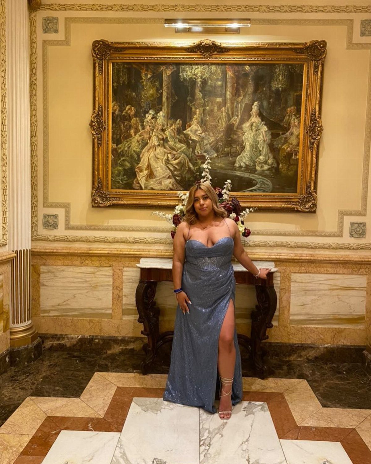 10 Nice Prom Dresses for Every Style and Body Type 4 Woman in a shimmering blue fitted strapless prom dress posing before a painting.