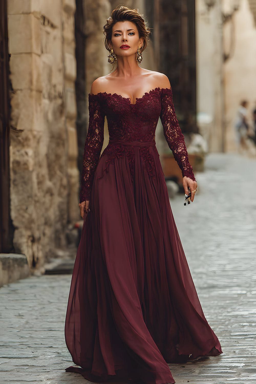 Woman in a burgundy lace bodice dress with a flowing chiffon skirt on cobblestones