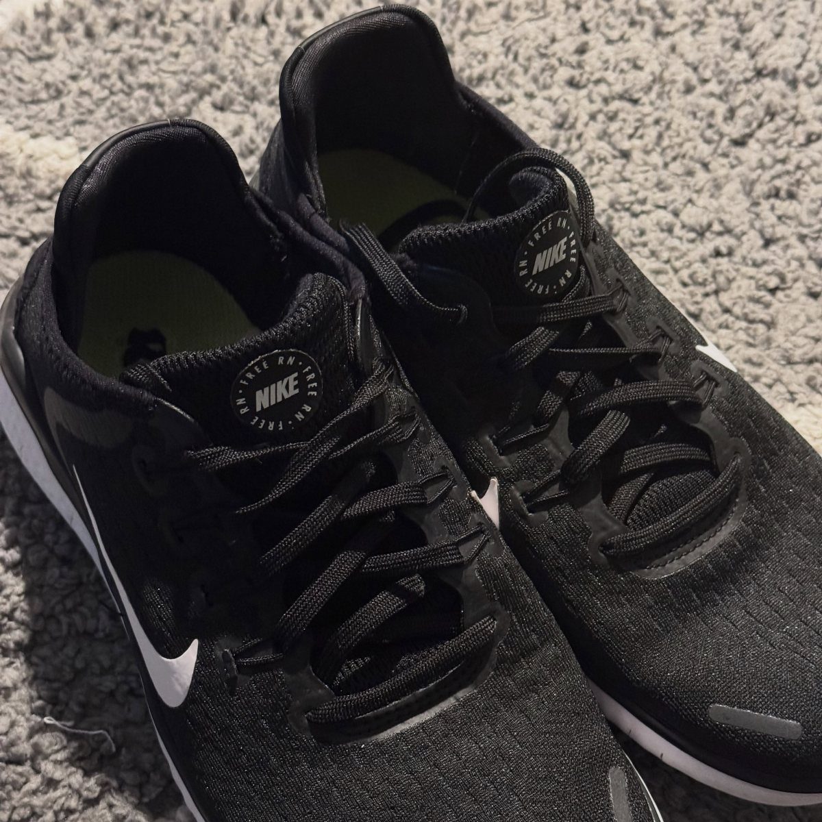 Nike Free Shoes: 7 Colorways and Styles to Wear Right Now 6 Black Nike Free sneakers with white logos resting on a grey textured carpet
