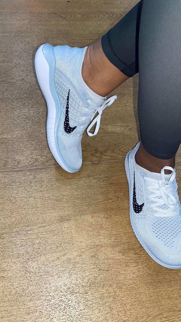 Nike Free Shoes: 7 Colorways and Styles to Wear Right Now 1 White Nike mesh sneakers with black swoosh logos on a wooden floor.