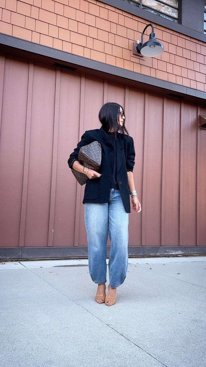 Woman wearing a black blazer and light blue wide-leg jeans with tan sandals.