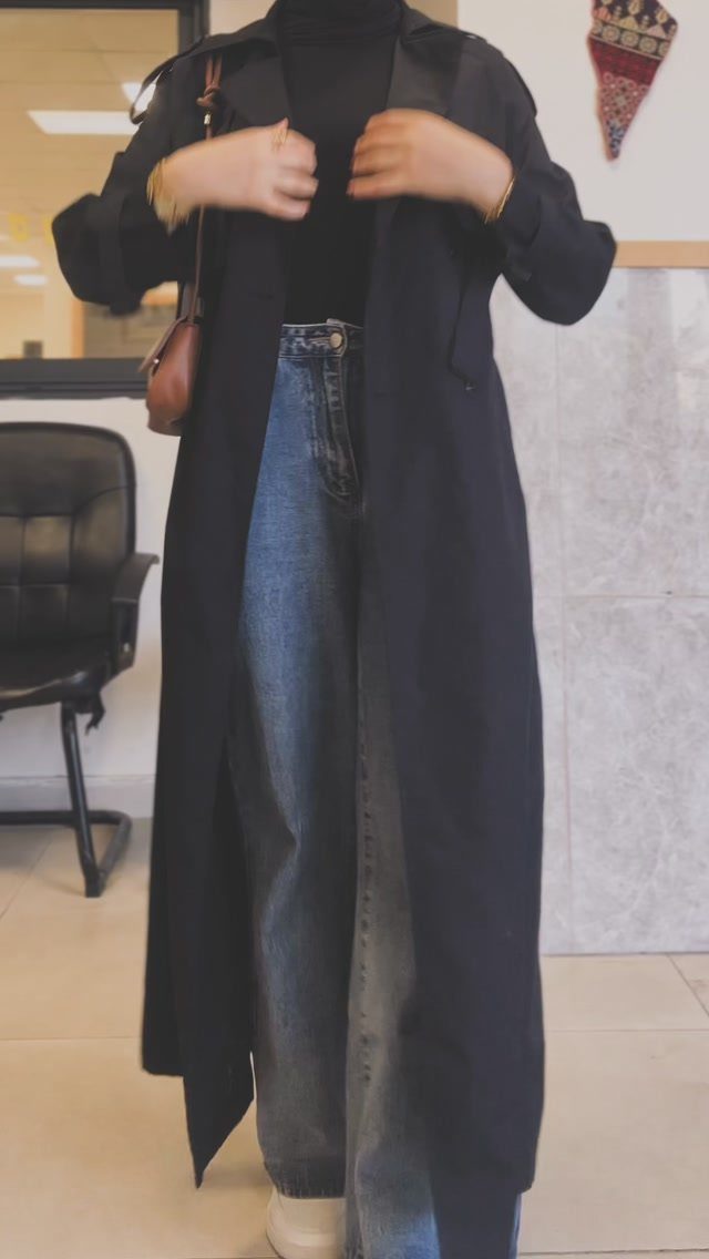 Person wearing a long black coat and wide-leg blue jeans in an office.