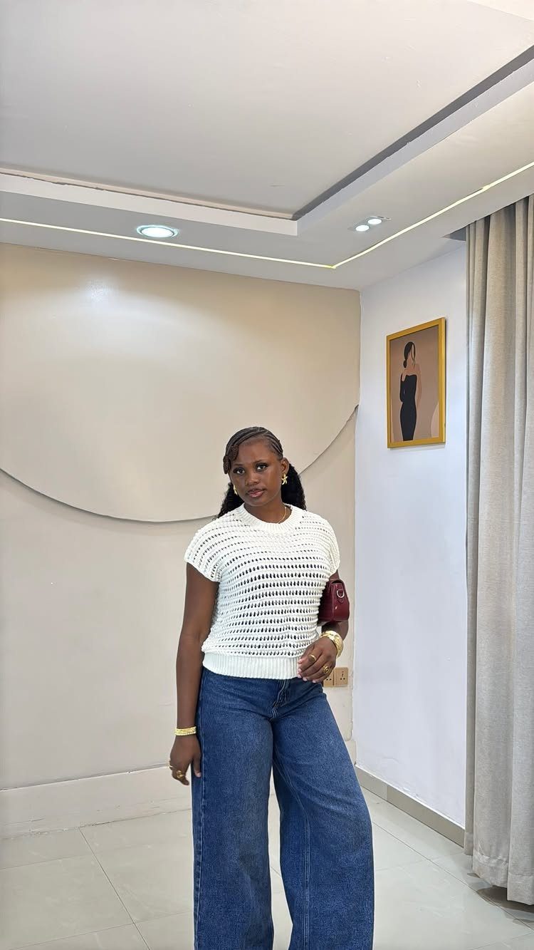Woman wearing a white crochet top and wide-leg blue jeans standing indoors.
