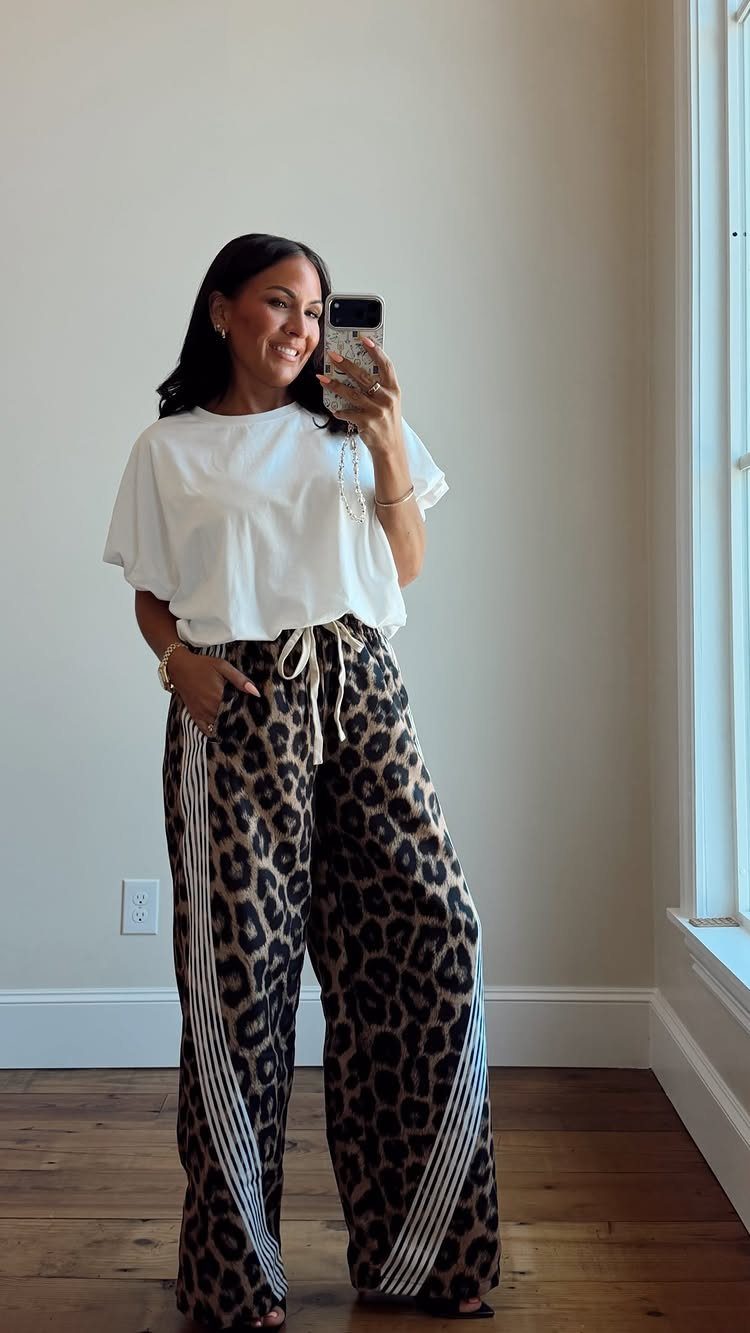 Woman in white t-shirt and leopard print wide-leg pants taking a mirror selfie.