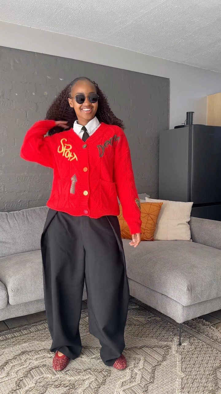 Woman in red cardigan and wide-leg black trousers posing in a living room.