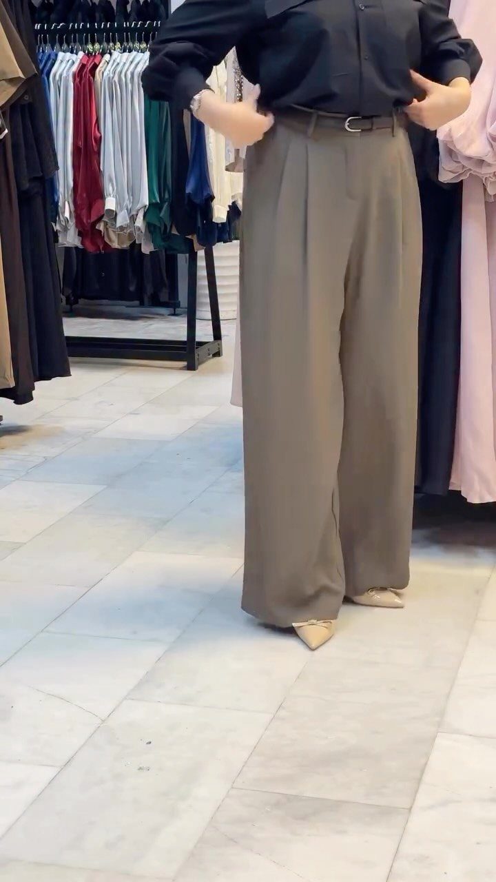 Person wearing a black shirt and wide-leg olive green trousers in a clothing store