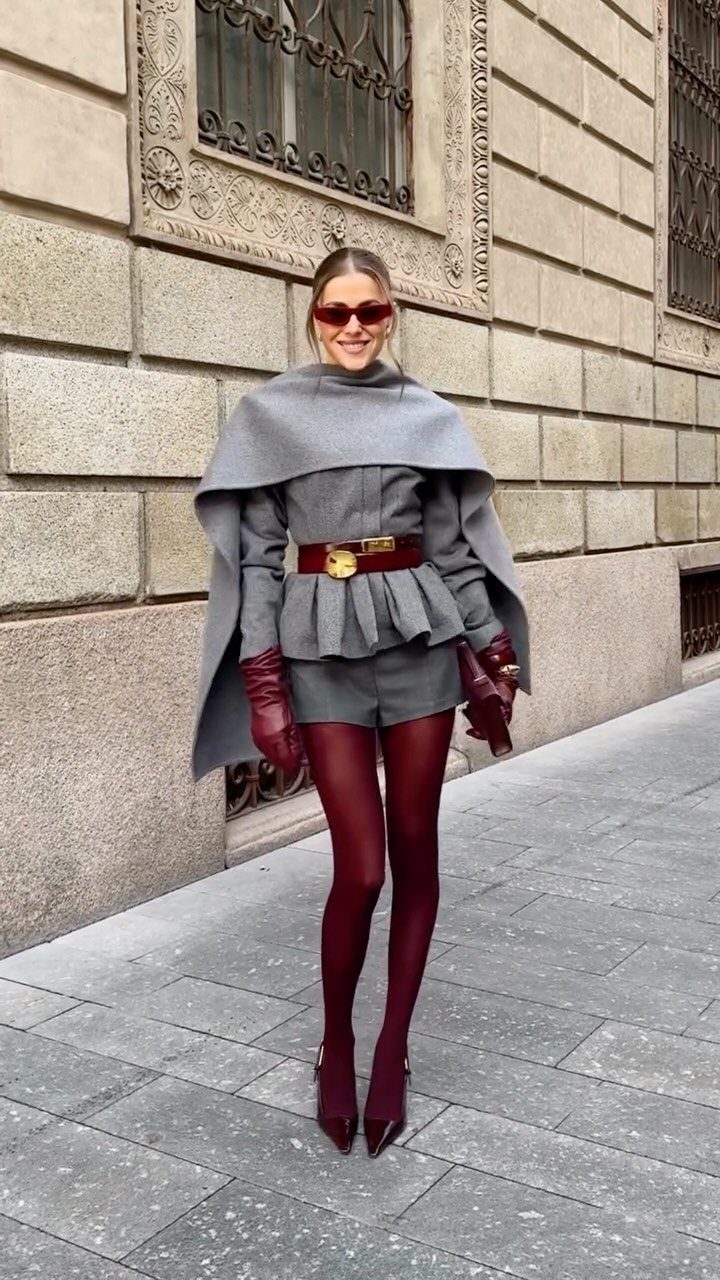 Woman in grey cape and shorts set with red tights and red accessories.