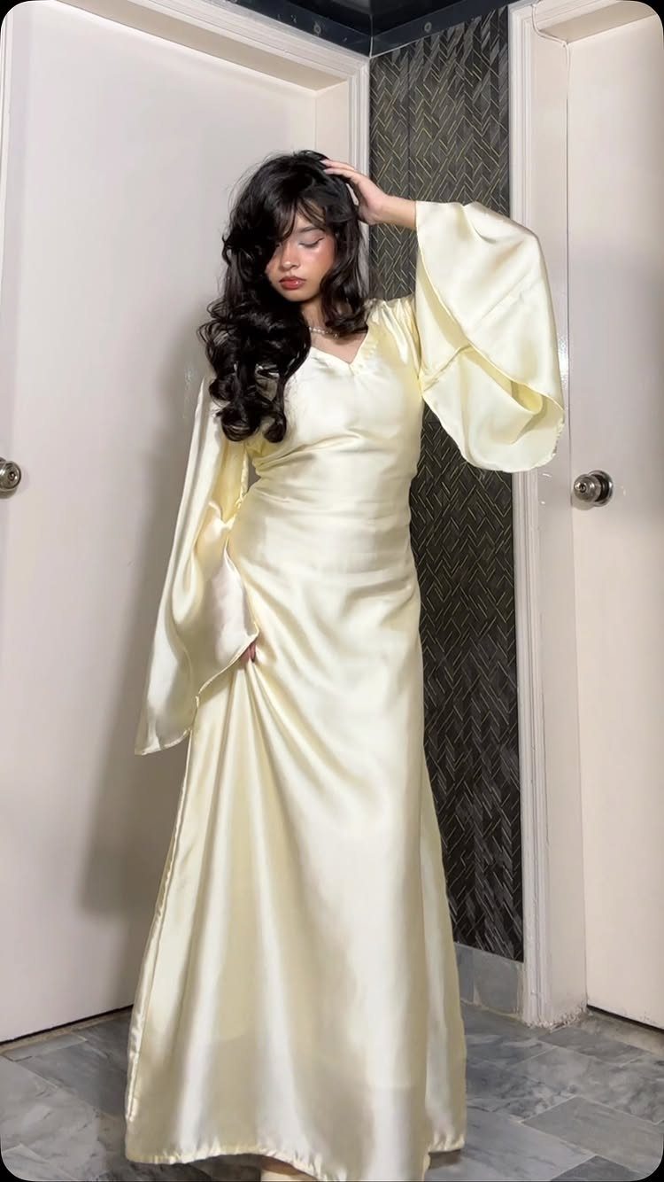 Woman in a long cream satin gown with puff sleeves posing indoors.