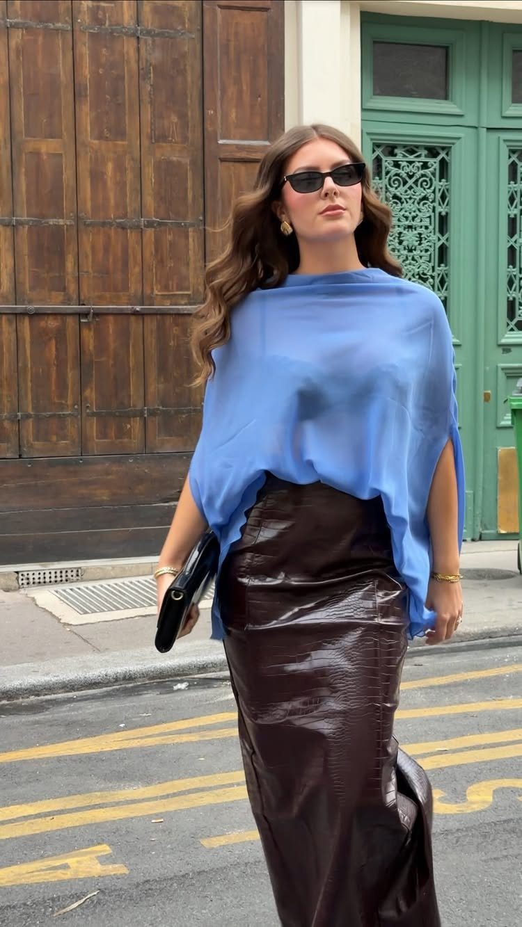 Woman wearing a sheer light blue statement blouse and brown crocodile skin skirt.