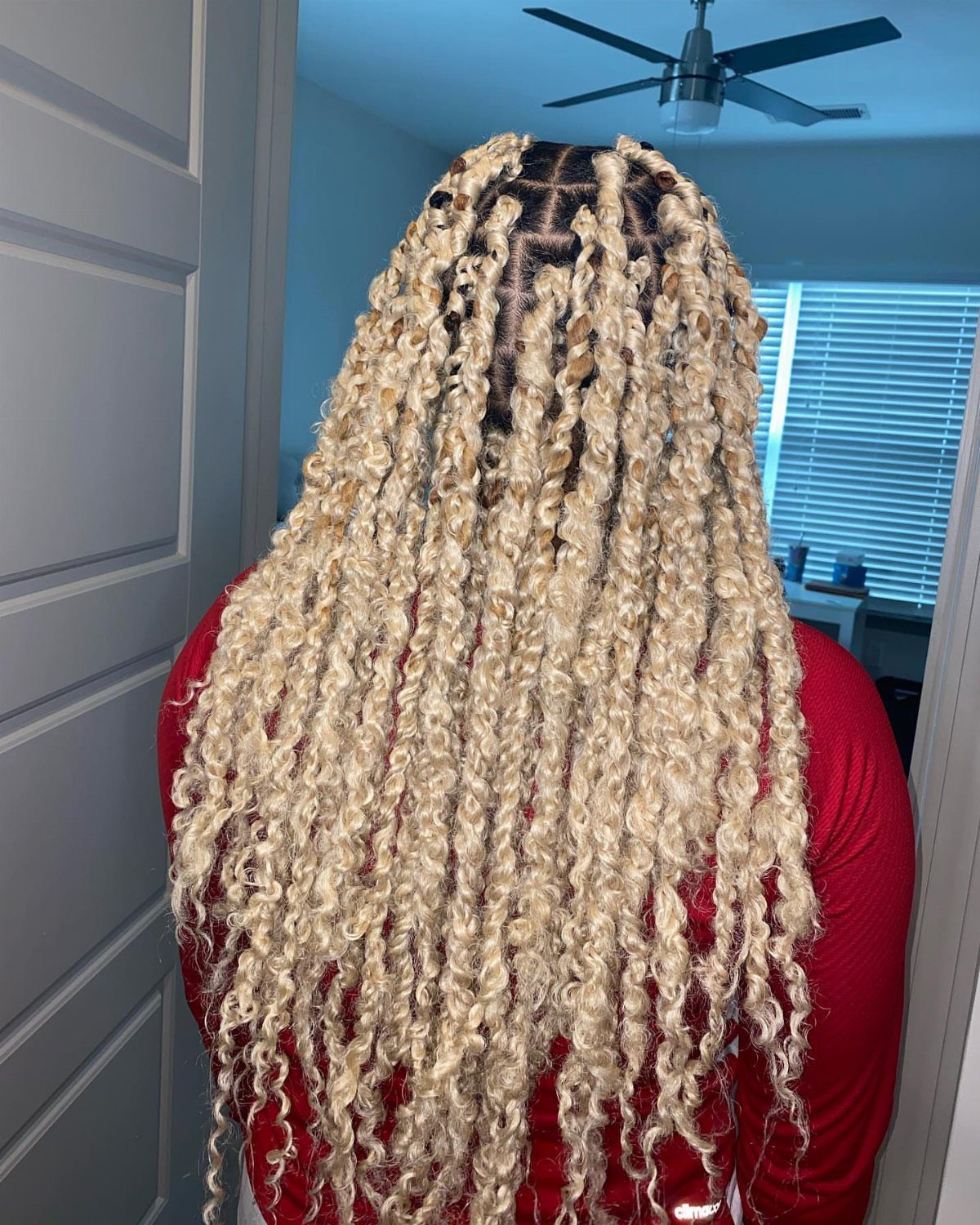 Long blonde passion twists falling over the back of a person in red.