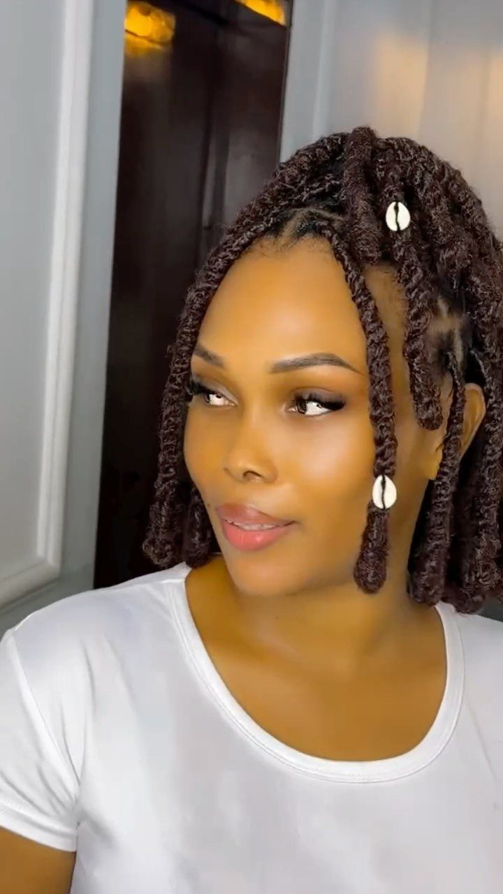 Woman with short dark brown passion twists adorned with white cowrie shell beads.