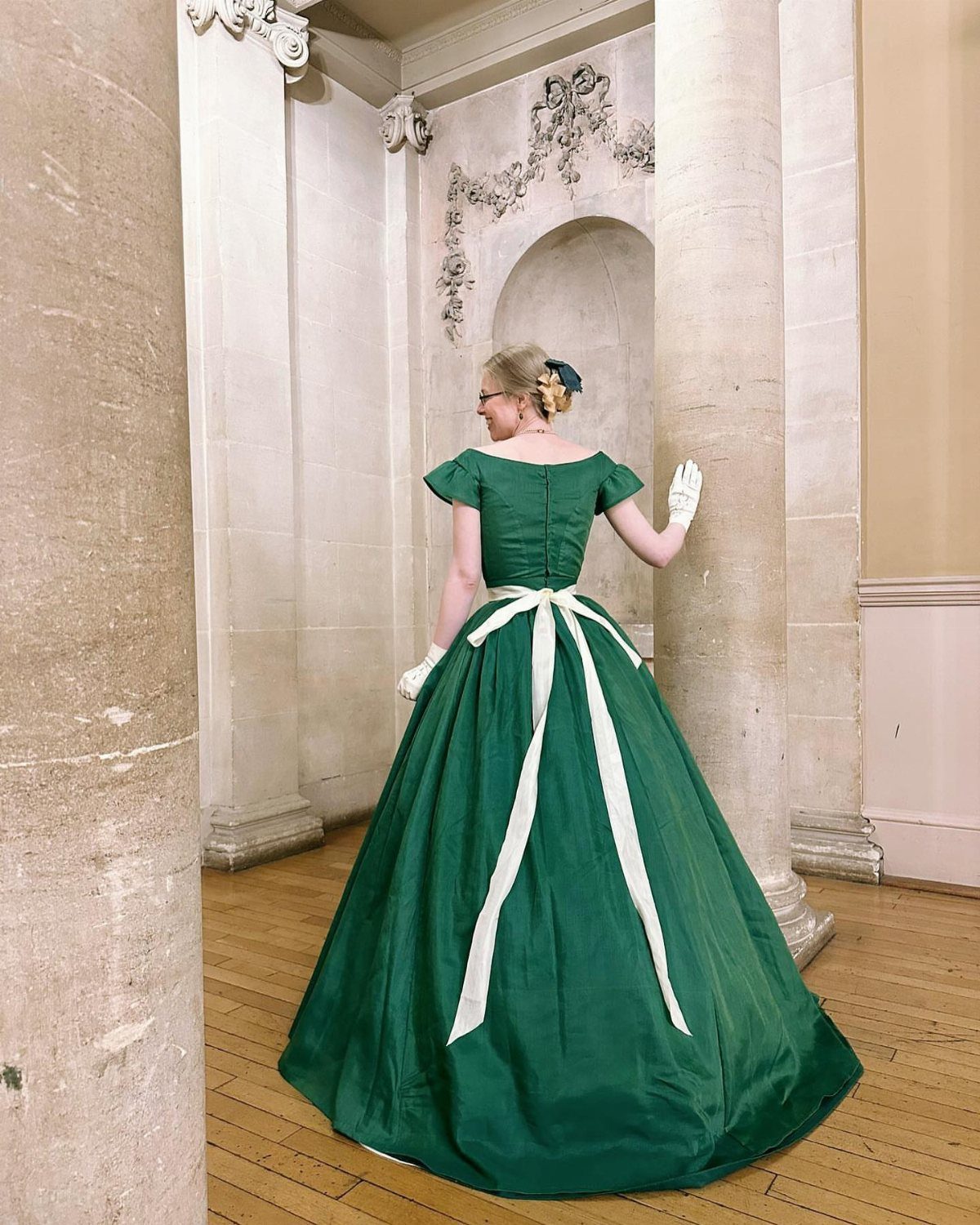 Period Piece Dresses: 5 Ideas, From Victorian to Steampunk 1 Woman in a green Victorian gown with white sash standing between stone columns.