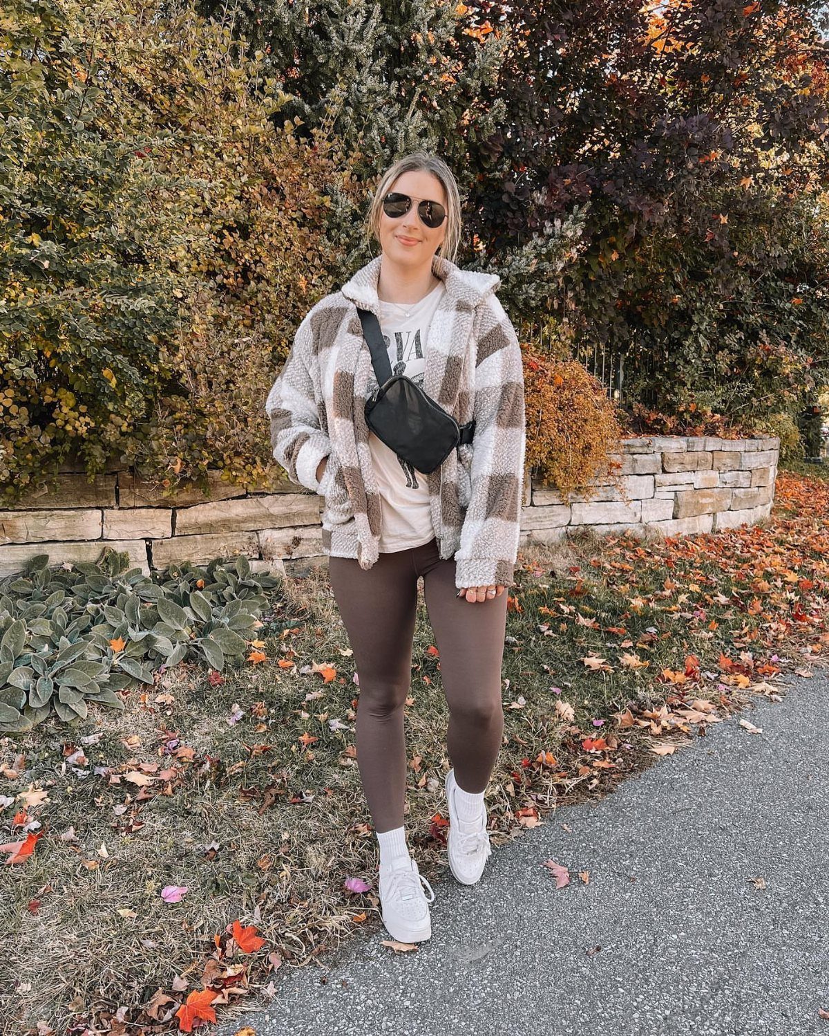 Woman wearing a plaid shacket, white t-shirt, brown leggings, and white sneakers outdoors.