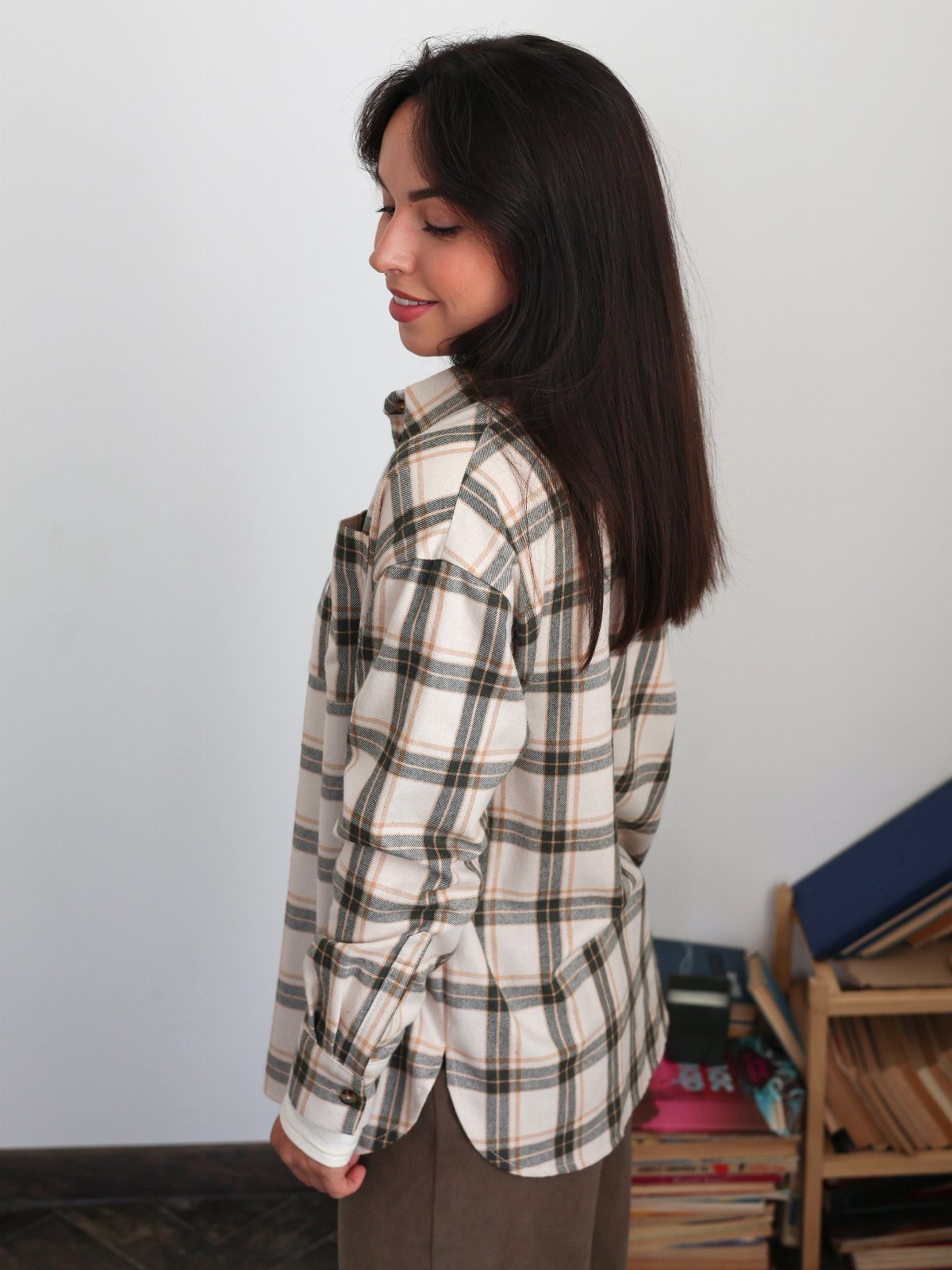 Woman wearing a white and brown plaid button-down shirt and brown pants.