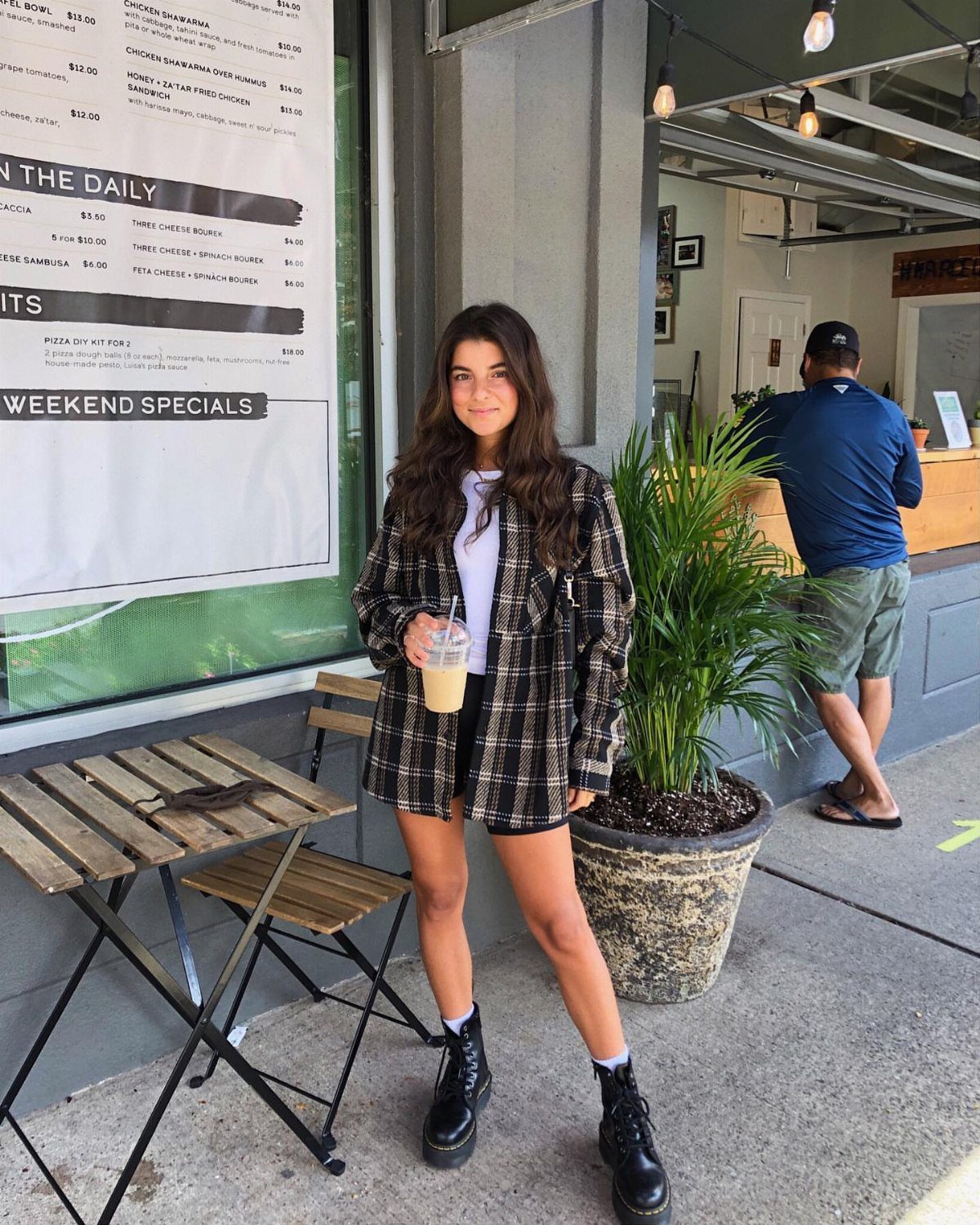 Woman wearing a black and white plaid shirt with denim shorts and combat boots.